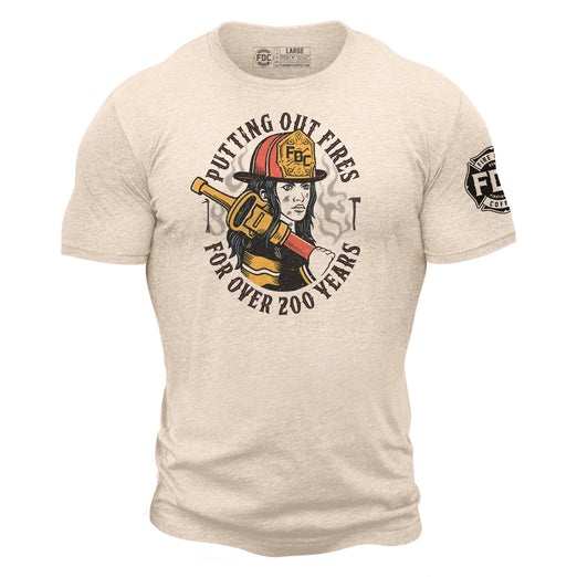 A tan t-shirt on a masculine figure with an image of a female firefighter and text around her that reads ”putting out fires for over 200 years”. FDC maltese cross logo is on one sleeve in black.